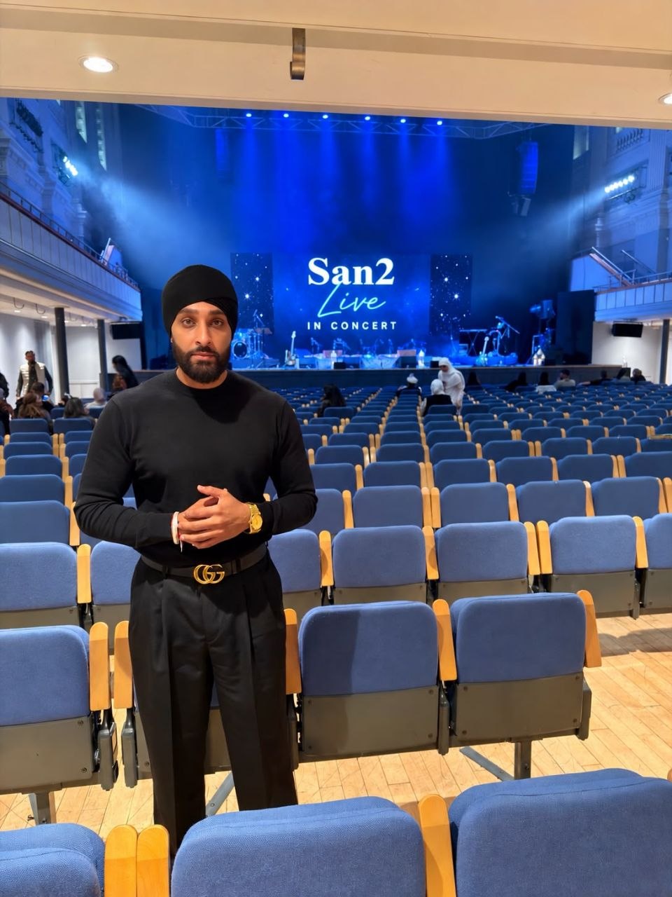 San2 standing in a concert hall with San2 Live on the stage screen